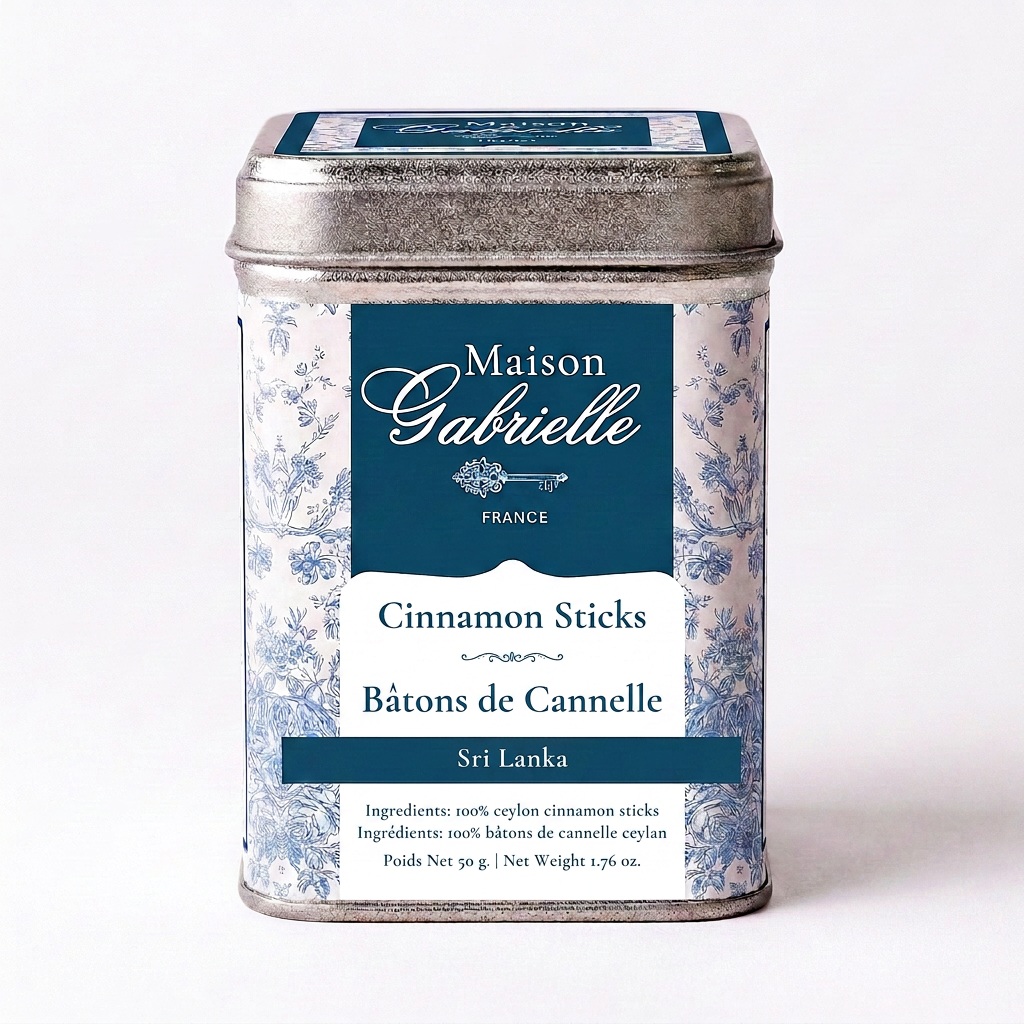A metal tin of Maison Gabrielle Cinnamon Sticks from Sri Lanka, featuring a blue and white floral pattern with a dark blue label, set against a plain white background.