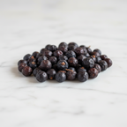 Macro Perspective Shot of Maison Gabrielle Whole Dried Juniper Berries on White Marble, Showcasing the Natural Matte Texture, Deep Purple Tones, and Authentic Botanical Detail