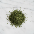 Maison Gabrielle Dried Parsley Flakes Piled on a White Marble Surface for Culinary Recipes and Seasoning