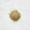 Overhead view of a mound of premium whole fennel seeds from Maison Gabrielle on a bright white marble surface, highlighting the spice's natural green and golden tones and ribbed texture.