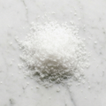 Overhead view of Maison Gabrielle's hand-harvested Fleur de Sel on a white marble surface, showcasing the delicate, crystalline texture and pure white quality of the finishing salt.