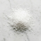Overhead view of Maison Gabrielle's hand-harvested Fleur de Sel on a white marble surface, showcasing the delicate, crystalline texture and pure white quality of the finishing salt.