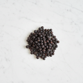 Top-Down View of Maison Gabrielle Premium Juniper Berries on a White Marble Background, Emphasizing the Contrast Between the Dark Berries and the Elegant Stone Surface