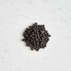 Top-Down View of Maison Gabrielle Premium Juniper Berries on a White Marble Background, Emphasizing the Contrast Between the Dark Berries and the Elegant Stone Surface