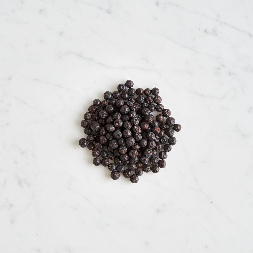Top-Down View of Maison Gabrielle Premium Juniper Berries on a White Marble Background, Emphasizing the Contrast Between the Dark Berries and the Elegant Stone Surface